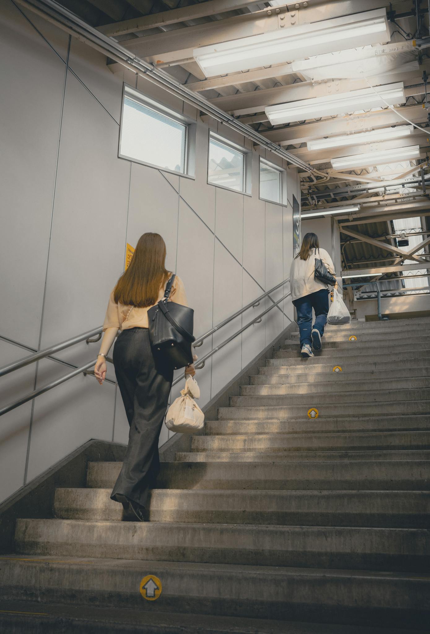 Two women walk up stairs in a modern Tokyo station, capturing urban life.